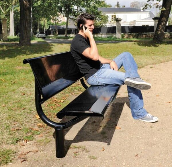 Photo illustrative d'un homme au téléphone assis sur un banc public perforé acier noir, dans un parc