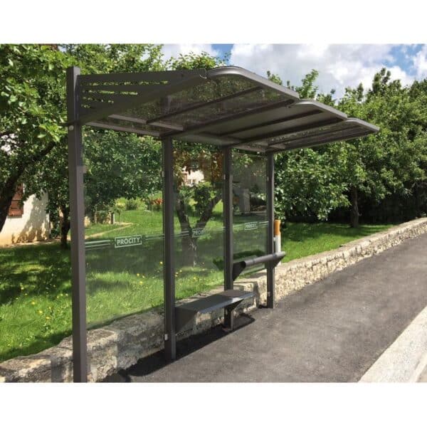Photo d'un abri bus convivial gris avec banc et assis-debout, sans affiche sur un trottoir, devant une maison