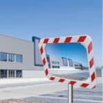 Photo illustrative d'un miroir industriel spécial hivers rectangulaire avec une bordure rouge et blanche rectangulaire, avec un bâtiment enneigé en arrière plan