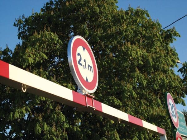 Photo de la fixation d'un panneau de limitation de hauteur sur un portique rouge et blanc