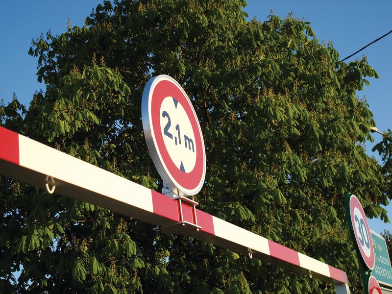 Photo de la fixation d'un panneau de limitation de hauteur sur un portique rouge et blanc