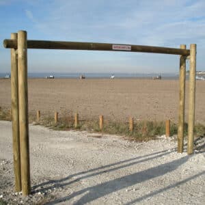 Photo d'un portique fixe en bois rond à l'entrée d'un chemin, avec une plage en arrière plan