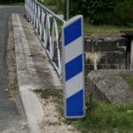 Photo d'une balise J13 de signalisation d'obstacle à rayures bleues et blanches avant un pont