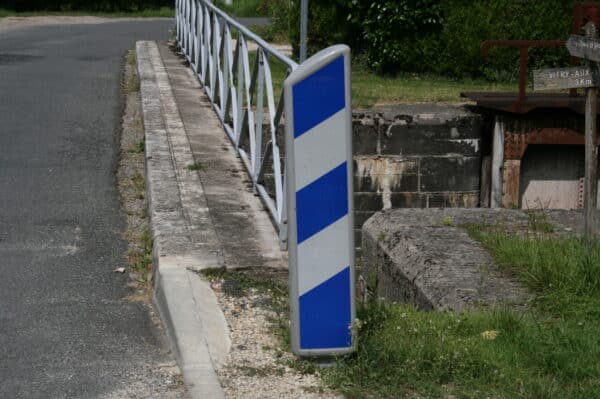 Photo d'une balise J13 de signalisation d'obstacle à rayures bleues et blanches avant un pont