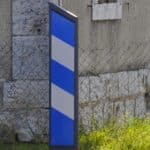 Photo d'une balise J13 de signalisation d'obstacle à rayures bleues et blanches au bord d'une route