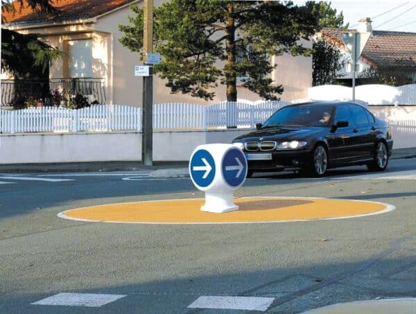 Photo d'une balise de contournement de giratoire, avec une voiture noire en arrière plan