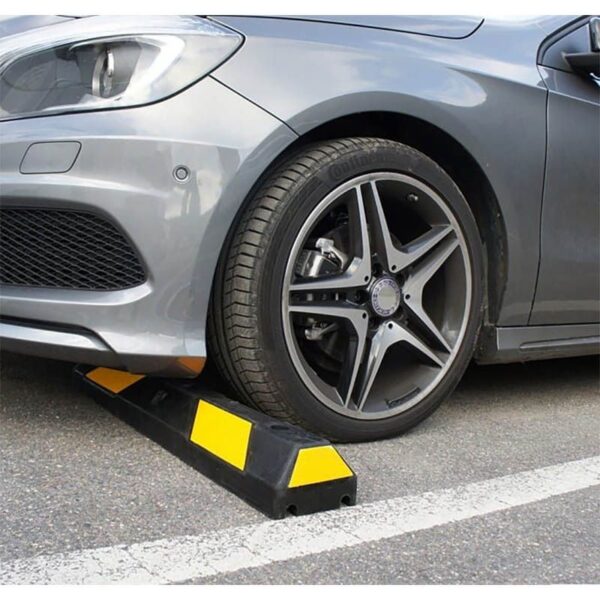 Photo d'illustration d'une voiture collée à une butée de parking en caoutchouc noire à bandes jaunes sur une place de parking