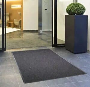 Photo d'un tapis professionnel d'extérieur 3 en 1 contre la saleté au pied d'une porte d'entrée noire d'immeuble