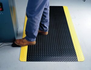 Photo d'une personne travaillant debout sur un tapis antifatigue haute performance noir et jaune