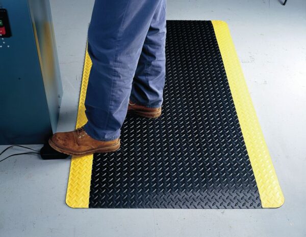 Photo d'une personne travaillant debout sur un tapis antifatigue haute performance noir et jaune
