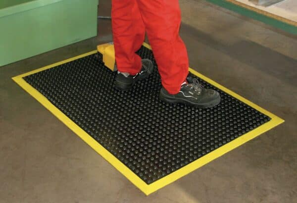 Photo d'une personne debout sur un tapis ergonomique antifatigue à bords jaunes