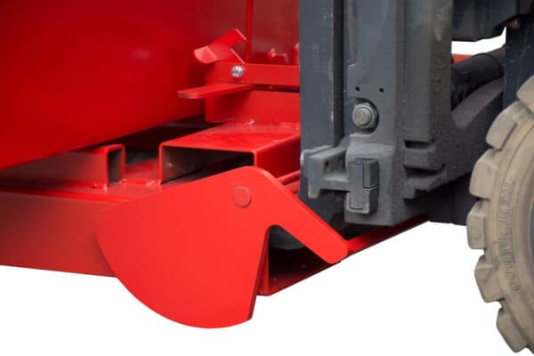 Photo gros plan de la fixation d'une benne basculante automatique rouge sur les lames d'un chariot élévateur